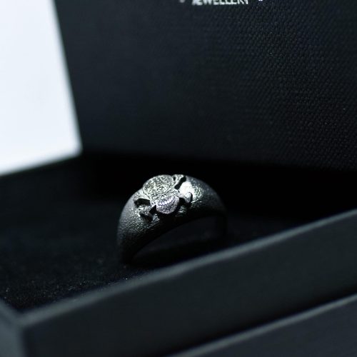 Ανδρικό δαχτυλίδι από ασήμι 925 βαθμών που έχει δεχθεί μαύρη επιπλατίνωση. Το δαχτυλίδι φέρει ένθετο έντεχνο χαρακτικό σχέδιο με νεκροκεφαλή. Δημιουργία της συλλογής Θυμήσου Σώμα