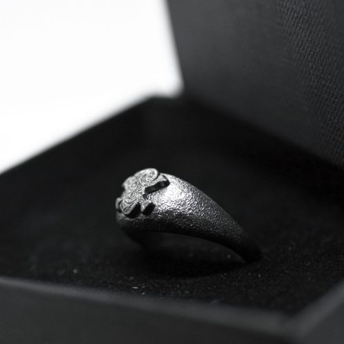 Ανδρικό δαχτυλίδι από ασήμι 925 βαθμών που έχει δεχθεί μαύρη επιπλατίνωση. Το δαχτυλίδι φέρει ένθετο έντεχνο χαρακτικό σχέδιο με νεκροκεφαλή. Δημιούργημα για τη συλλογή Θυμήσου Σώμα