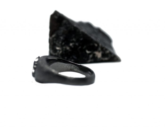 Ανδρικό δαχτυλίδι από ασήμι 925 βαθμών που έχει δεχθεί μαύρη επιπλατίνωση. Το δαχτυλίδι φέρει ένθετο έντεχνο χαρακτικό σχέδιο με νεκροκεφαλή. Κομμάτι της συλλογής ''Θυμήσου Σώμα''